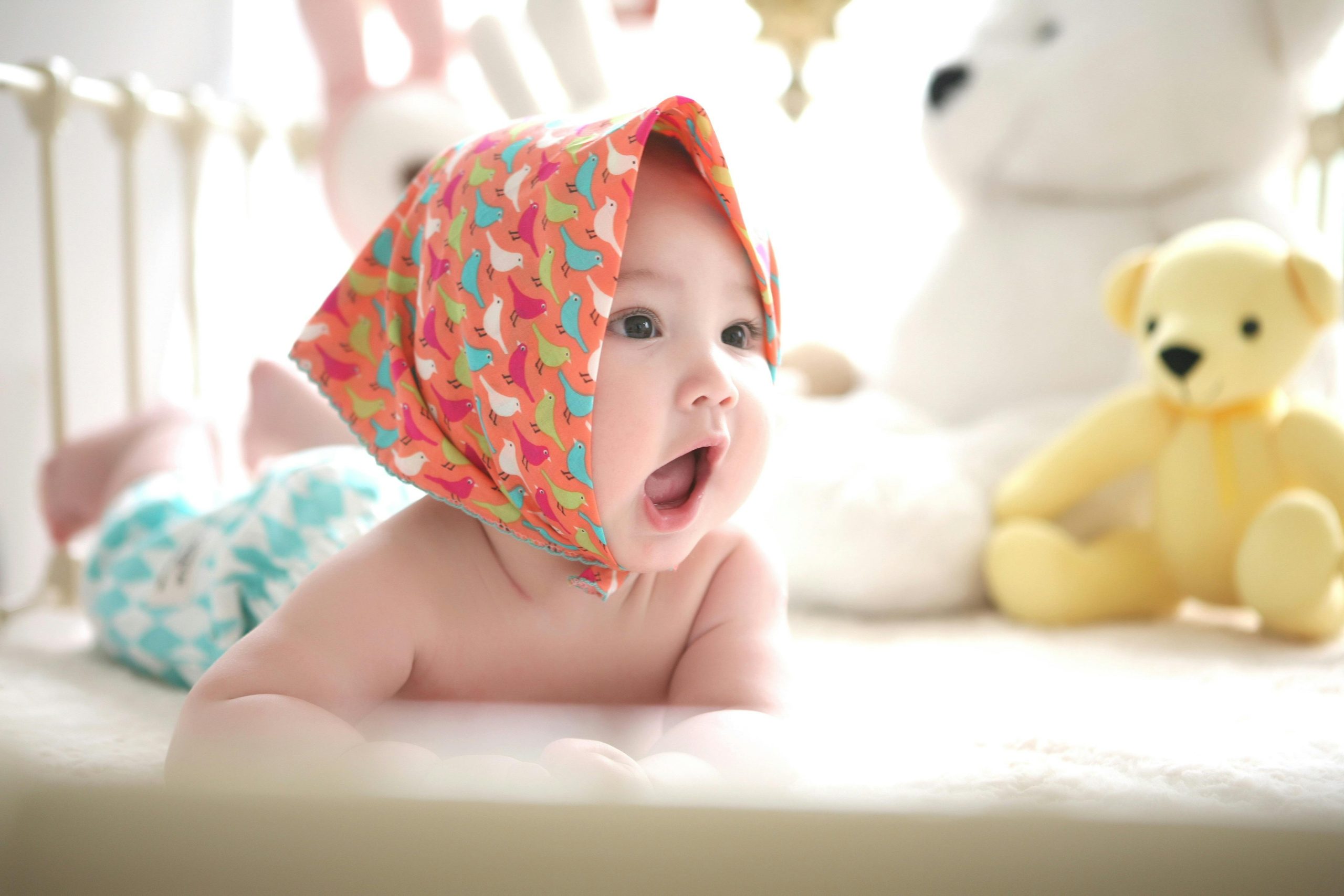 Charming baby with colorful scarf surrounded by cute plush toys, highlighting innocence indoors.