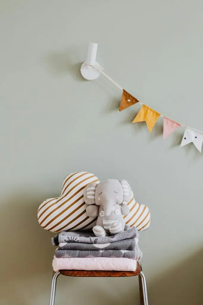 A cozy nursery setting with folded blankets, pillows, and an elephant toy on a chair.